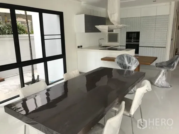 Detached House for rent in Bang Kapi, Bangkok - Bright open-plan kitchen with island, built-in oven and dining table beside sliding glass doors.