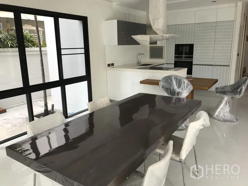 Detached House for rent in Bang Kapi, Bangkok - Bright open-plan kitchen with island, built-in oven and dining table beside sliding glass doors.