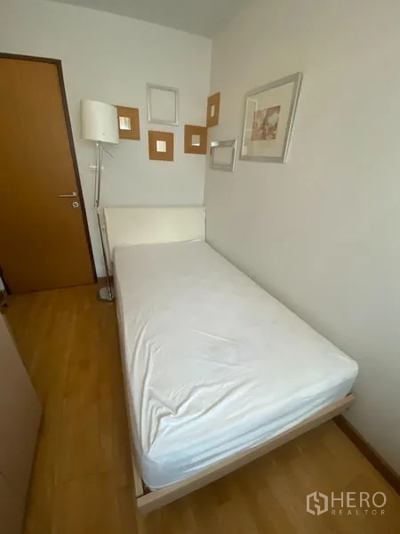 Condominium for rent or sale in Khlong Toei, Bangkok - Single-bed room with wall art, floor lamp and warm wood floors.