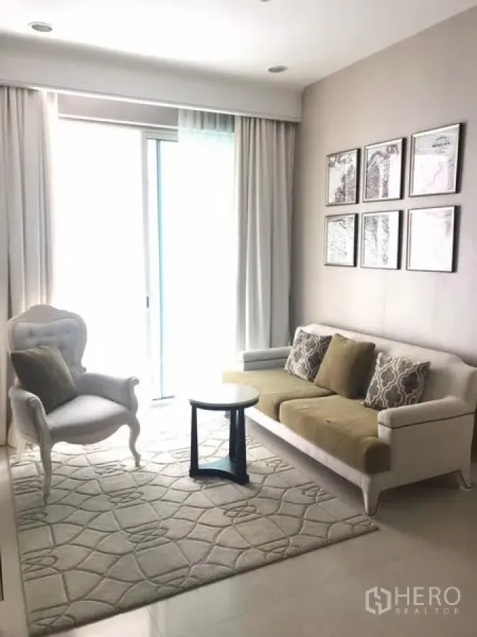 公寓 出租在Pathum Wan, Bangkok - 明亮客厅，白色沙发与扶手椅，几何地毯，落地推拉玻璃门与纱帘。