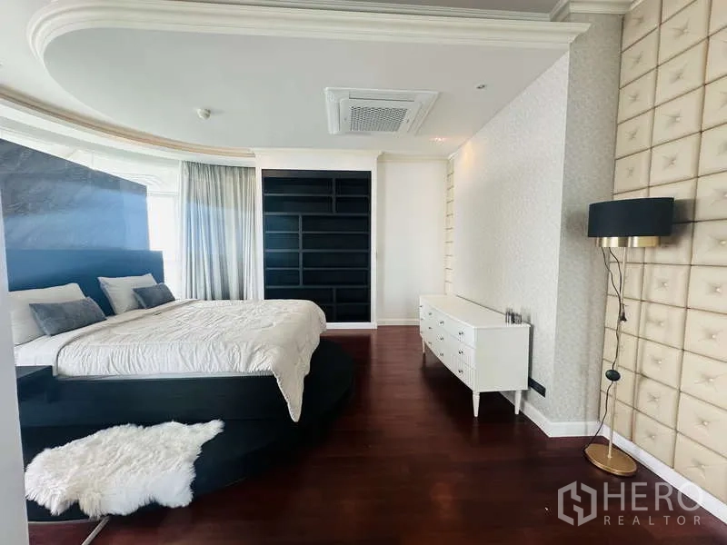 Condominium for rent or sale in Khlong Toei, Bangkok - Master bedroom angle showing platform bed, black shelving wall, floor lamp and timber flooring.