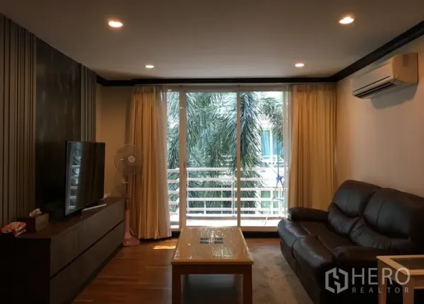 Condominium for sale in Khlong Toei, Bangkok - Bright living room with leather sofa, TV console and sliding doors opening to a balcony with palm views.