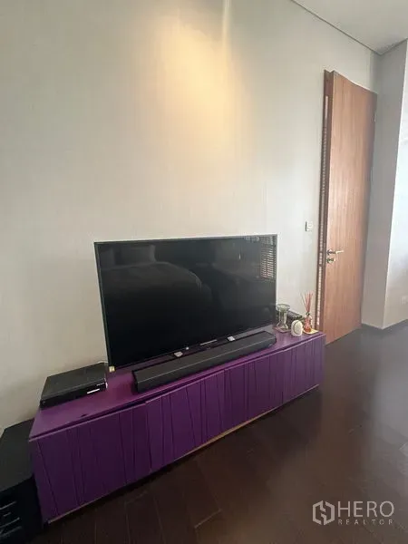 Condominium for rent or sale in Sathon, Bangkok - Flat-screen TV on a modern purple media console beside a wooden door.
