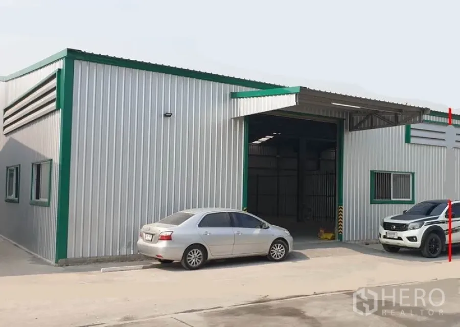 货栈 出租在Pak Kret, Nonthaburi - 金属板外墙与绿色装饰的仓库外观，宽卷帘门与停车区。