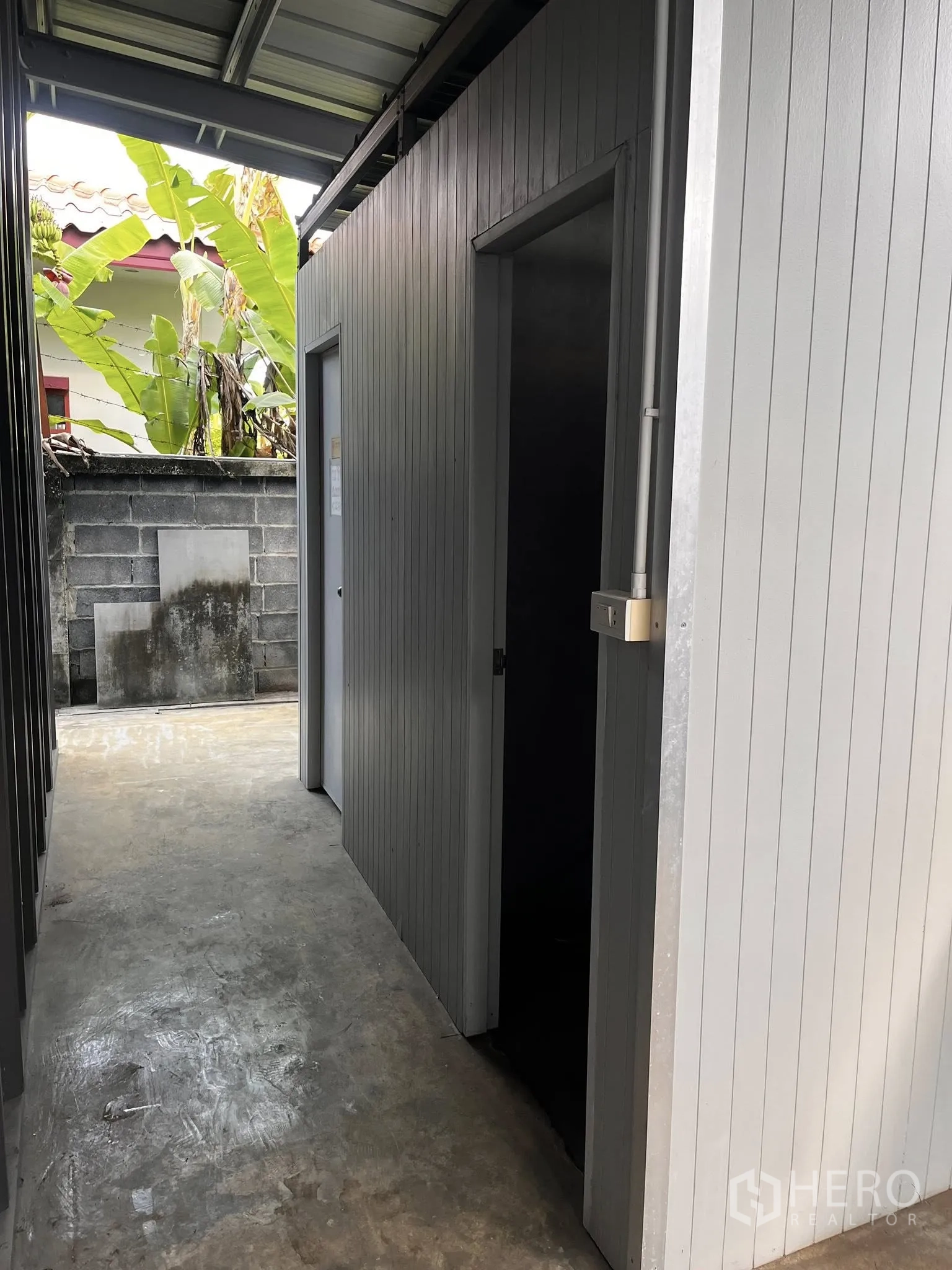 Warehouse for rent in Lat Phrao, Bangkok - Side corridor with service rooms under a roof beside a boundary wall.