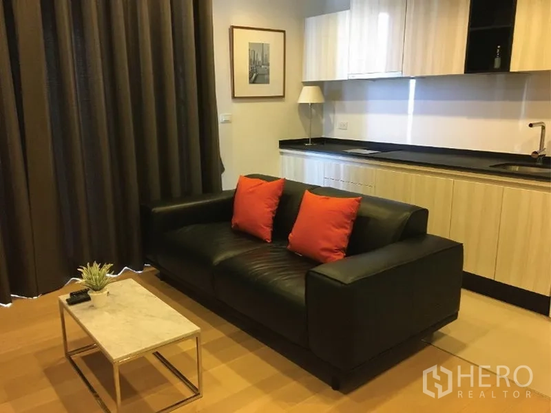 公寓 出租或出售在Watthana, Bangkok - 开放式客厅，黑色皮沙发、大理石茶几与时尚一字型厨房。