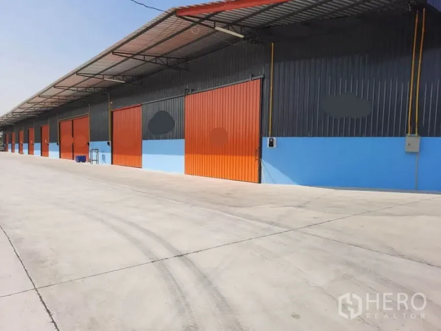 Warehouse for rent in Khlong Luang, Pathum Thani - Row of modern warehouse bays with bright orange sliding doors, covered loading canopy and wide concrete driveway in Khlong Luang.