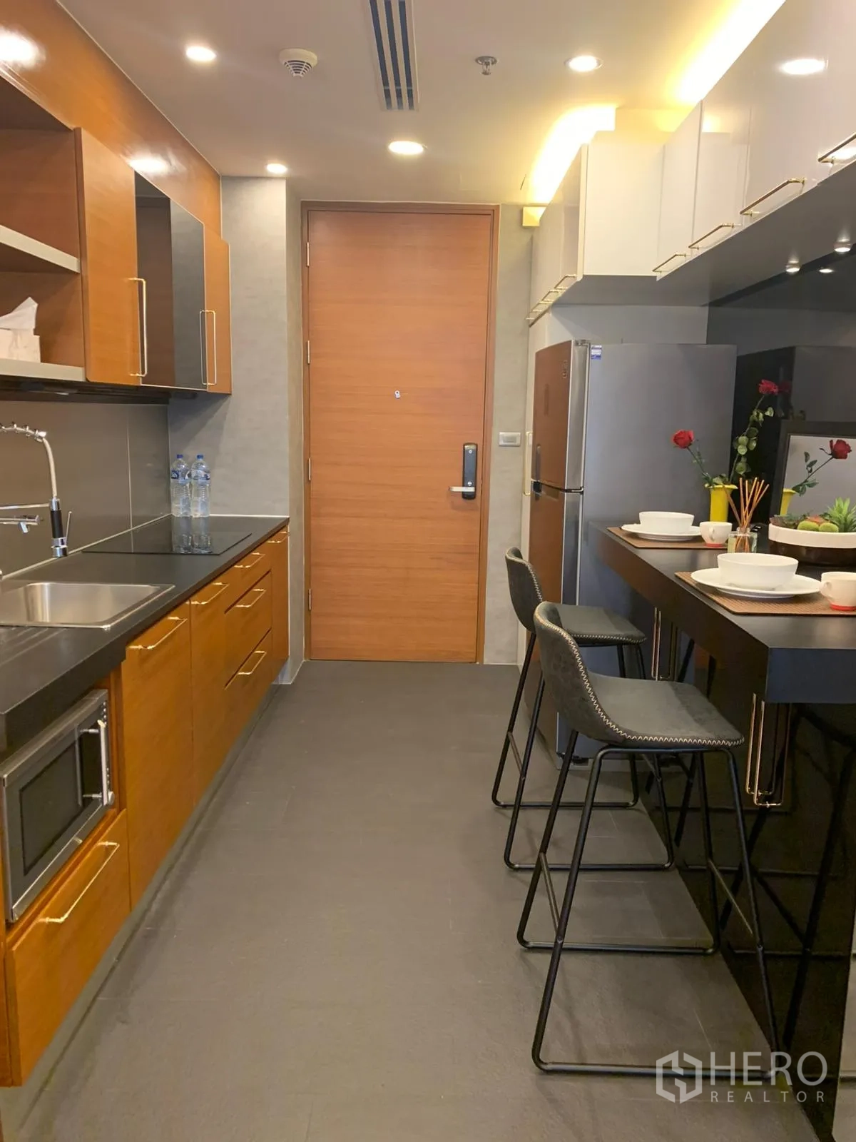 Condominium for sale in Khlong Toei, Bangkok - Modern galley kitchen with wood cabinets, breakfast bar and stainless refrigerator.