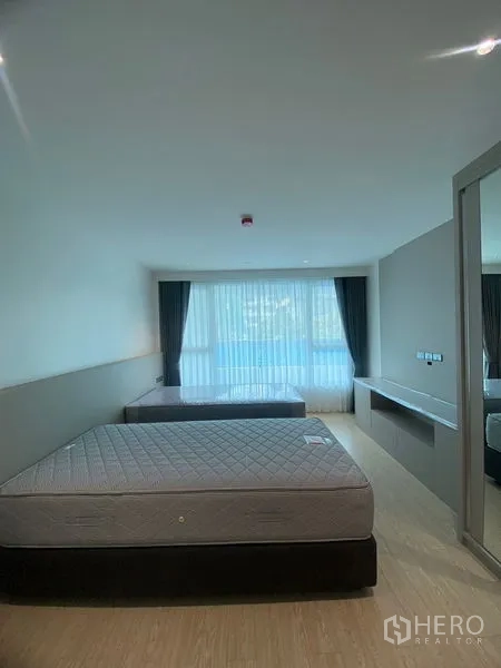 Apartment for rent in Watthana, Bangkok - Second bedroom with two beds, full‑width window with sheer curtains and a mirrored wardrobe.