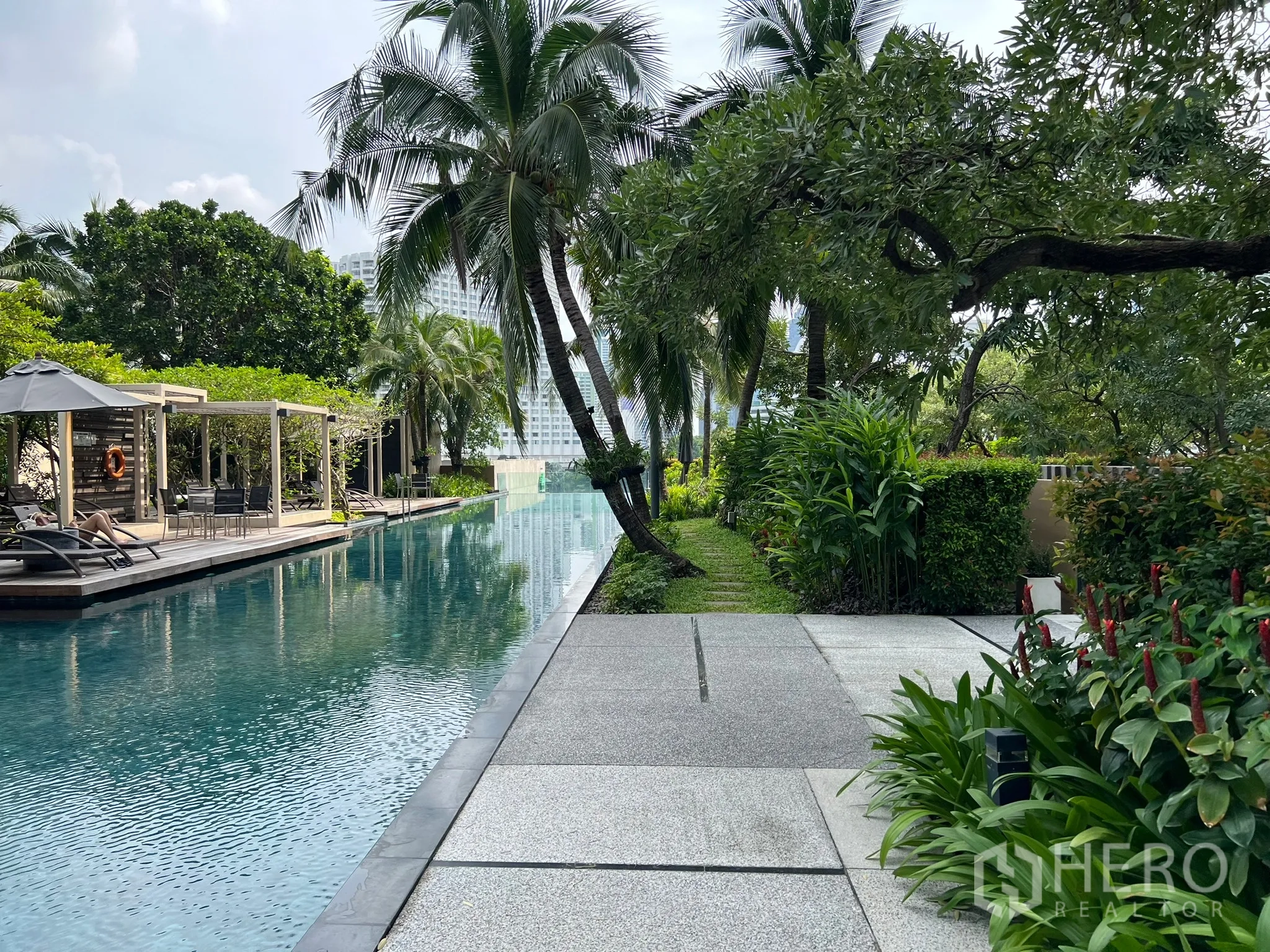 Condominium for sale in Khlong San, Bangkok - Lush garden pathway beside a long swimming pool with sun loungers and cabana.