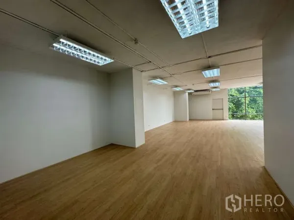 Office Space for rent in Sathon, Bangkok - Long view of open workspace with column, wood flooring, multiple ceiling lights and full-height windows to trees.