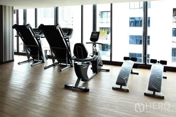 Condominium for rent or sale in Pathum Wan, Bangkok - Condo fitness room with treadmills, exercise bike and ab benches beside large windows overlooking Bangkok.