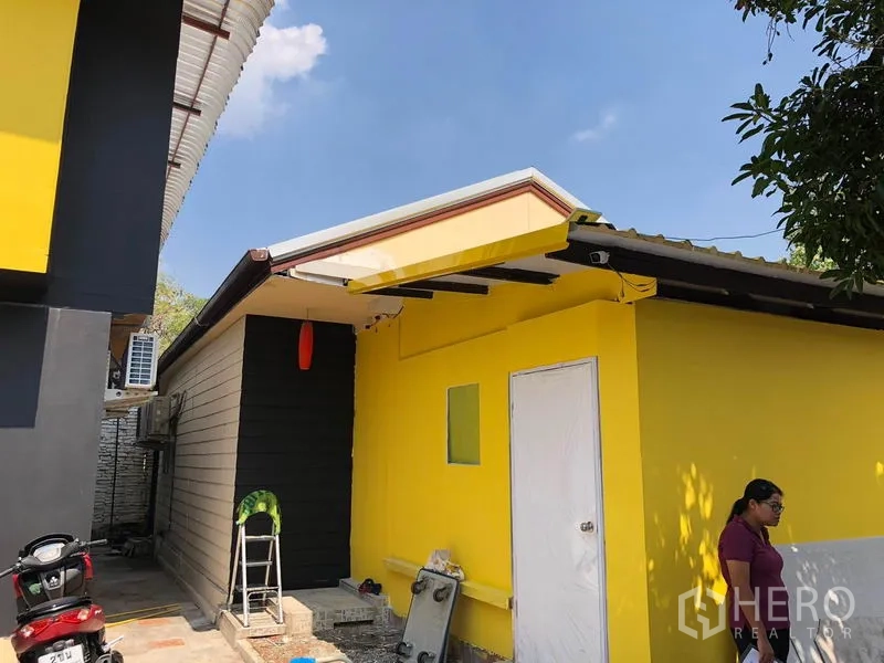 独立式住宅 出售在Khlong Toei, Bangkok - 主楼旁的单层附属建筑，黄色外墙、白色门和钢制雨篷。