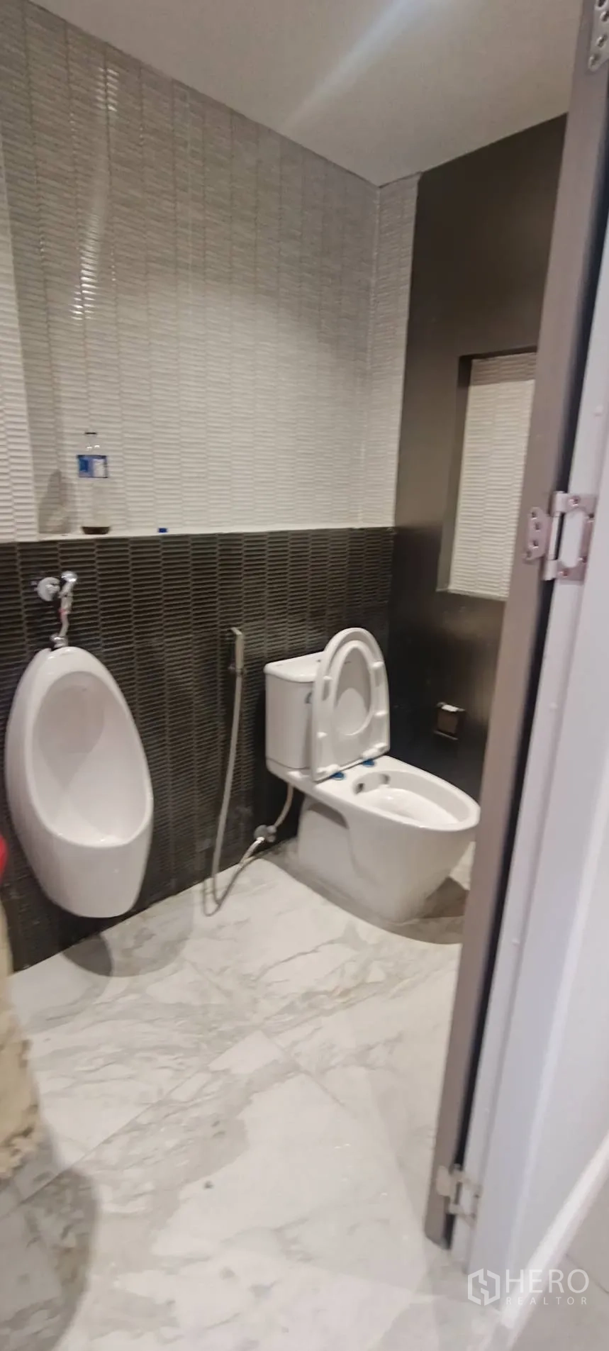 Office Space for rent in Watthana, Bangkok - Restroom with urinal and toilet, dark tile wall, and marble-look floor.