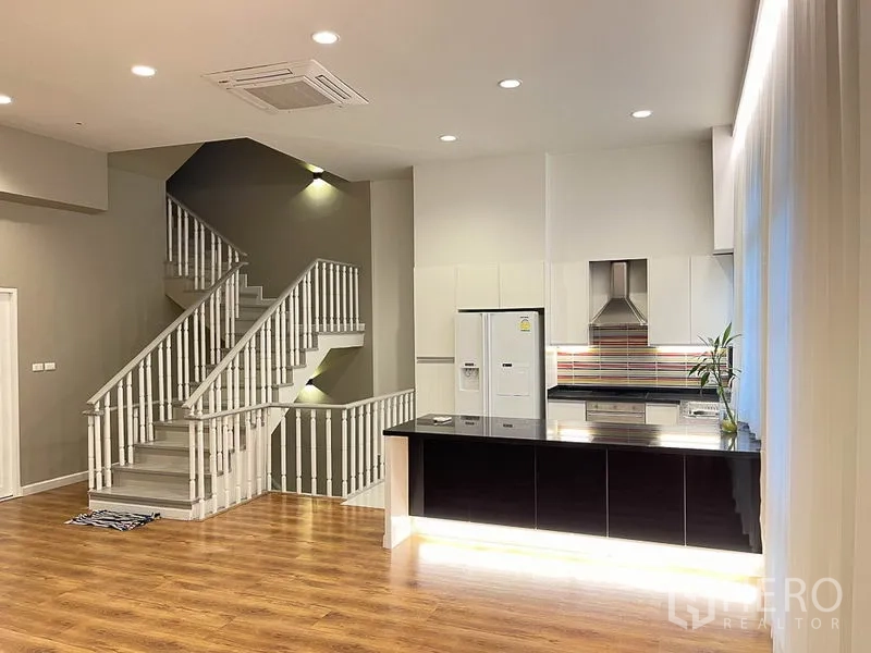 Townhouse for rent in Yan Nawa, Bangkok - Contemporary kitchen beside a white staircase with accent lighting and glossy black breakfast bar.