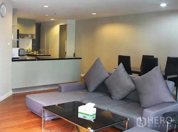 คอนโด ให้เช่าในHuai Khwang, Bangkok - ห้องนั่งเล่นเปิดโล่ง โซฟาเข้ามุมสีเทา โต๊ะกระจก และพื้นไม้ ใกล้ครัวสมัยใหม่