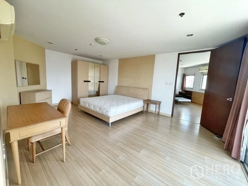 Condominium for rent in Khlong Toei, Bangkok - Spacious bedroom with double bed, wardrobe, desk and wood flooring.
