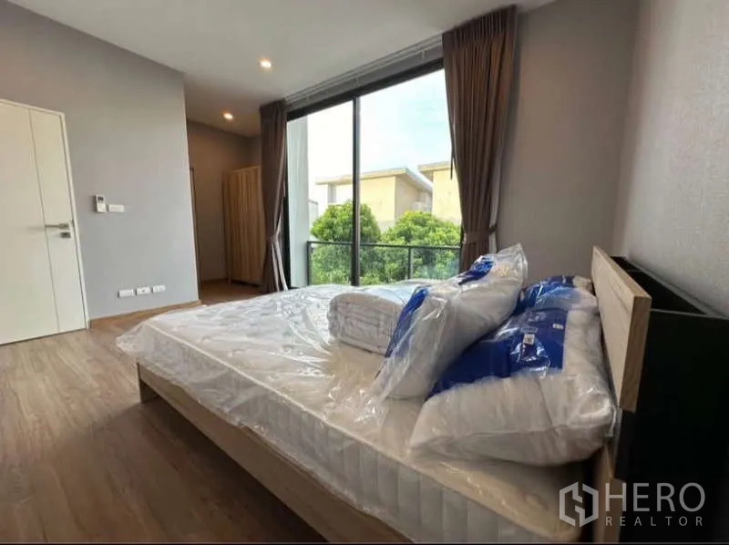 Townhouse for rent in Lat Phrao, Bangkok - Master bedroom with sliding glass doors to a balcony and garden outlook.