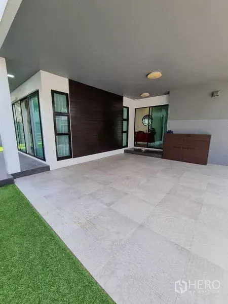 Detached House for rent or sale in Prawet, Bangkok - Covered carport or terrace with tiled floor beside glass sliding doors and lawn.