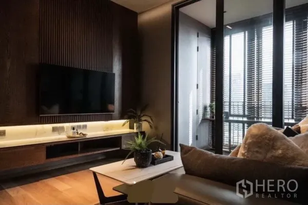 Condominium for rent in Khlong Toei, Bangkok - Built-in TV wall with ribbed wood paneling and LED shelf lighting beside full-height glass doors.