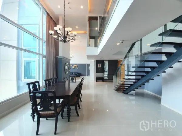 公寓 出租在Ratchathewi, Bangkok - 挑高双层餐区，悬挂吊灯，落地窗，玻璃栏杆楼梯通往夹层。