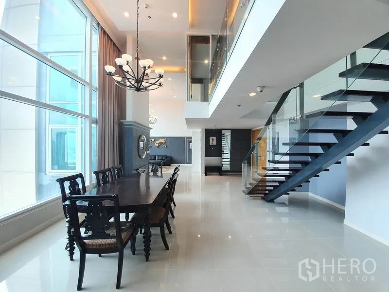 公寓 出租在Ratchathewi, Bangkok - 挑高双层餐区，悬挂吊灯，落地窗，玻璃栏杆楼梯通往夹层。