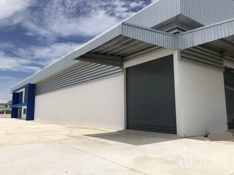 Warehouse for rent in Samut Prakan - Covered loading bay with grey roller shutter door and metal canopy.