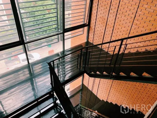 公寓 出租在Watthana, Bangkok - 采光良好的楼梯间，黑色金属楼梯、红砖墙与落地百叶窗。