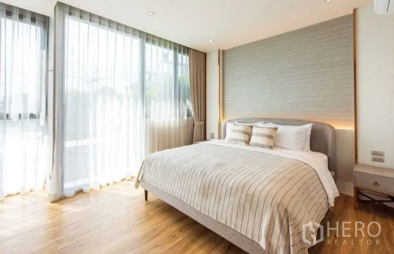 公寓 出租在Bang Na, Bangkok - 采光充足的卧室，配有大床、装饰墙、纱帘与木质地板。