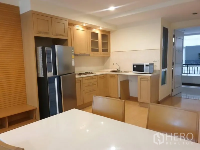 Condominium for rent in Watthana, Bangkok - Light-wood kitchen with upper cabinets, cooktop, microwave and double-door fridge.