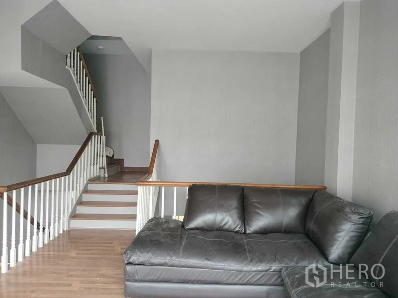 Townhouse for rent in Bueng Kum, Bangkok - Staircase landing with black leather sofa and white balustrade.