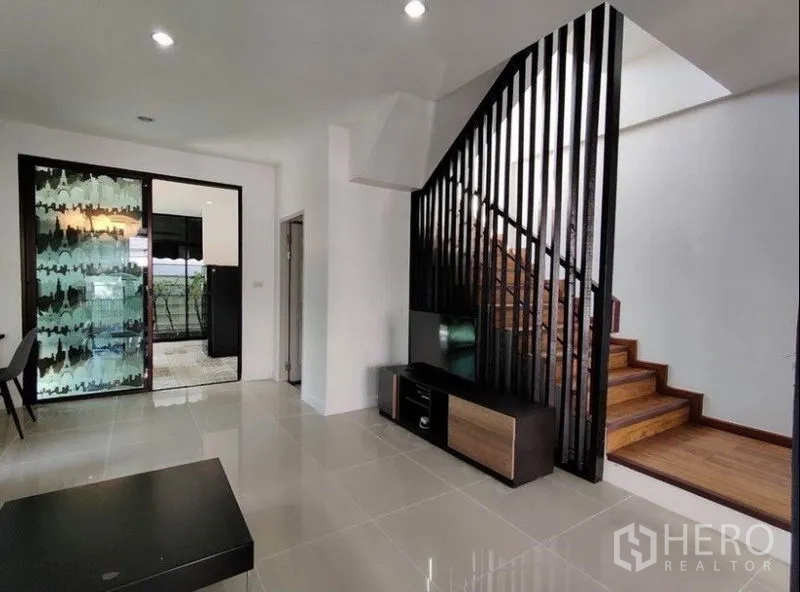 Townhouse for rent in Suan Luang, Bangkok - Living area facing a wooden staircase with black vertical slats.