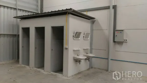 Warehouse for rent in Lam Luk Ka, Pathum Thani - On-site restroom block inside the warehouse with stalls, twin sinks, mirrors and an electrical control panel.