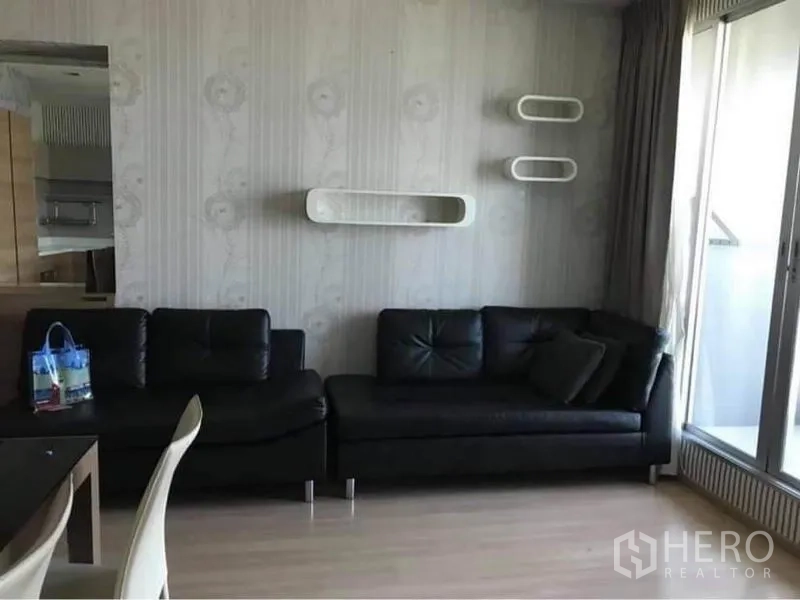 Condominium for rent or sale in Phaya Thai, Bangkok - Bright living room with black leather sofa, floating shelves and sliding door to a balcony.