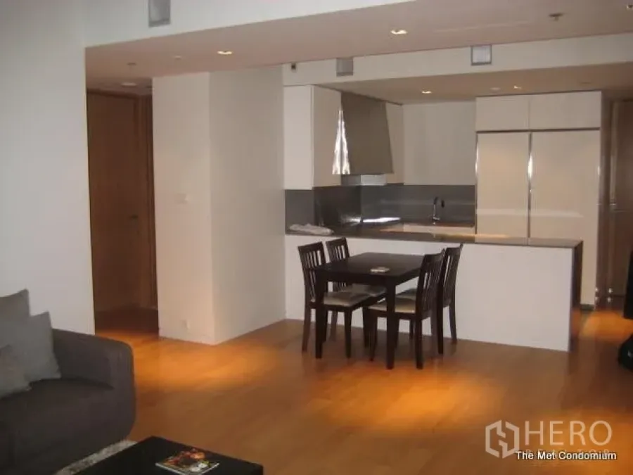 Condominium for rent or sale in Sathon, Bangkok - Open-plan living and dining area with wood floors facing a sleek kitchen and island in a modern Sathon condo.