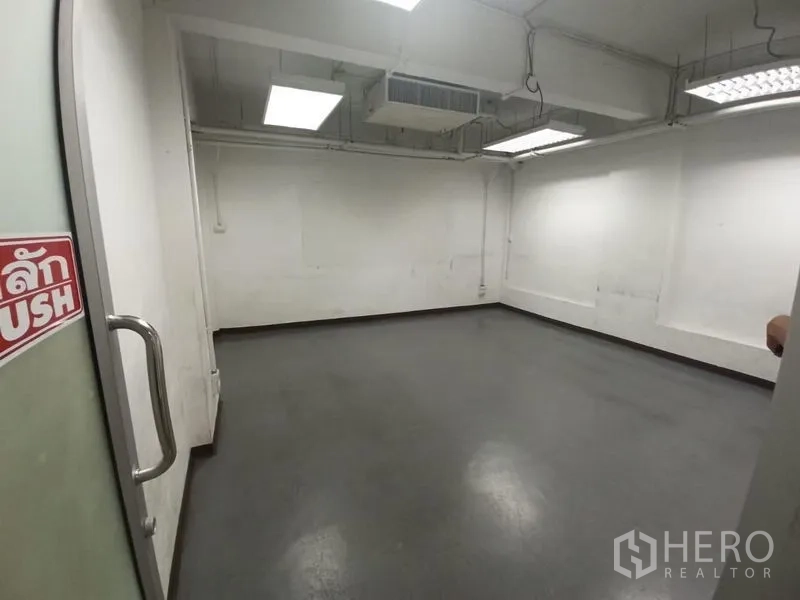 Office Space for rent in Ratchathewi, Bangkok - Empty office room with gray flooring, white walls, exposed ceiling and fluorescent lighting.