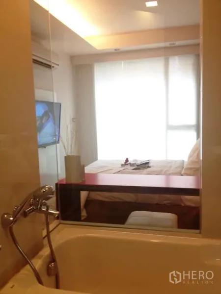 公寓 出租在Watthana, Bangkok - 浴室设浴缸与玻璃隔断，可望向明亮卧室与大窗。