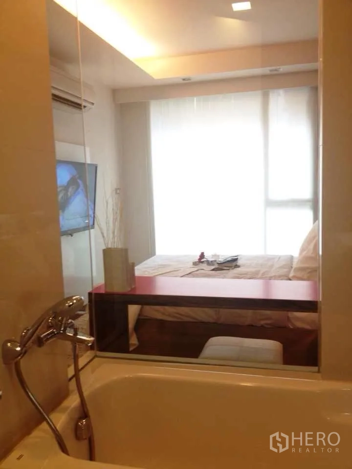公寓 出租在Watthana, Bangkok - 浴室设浴缸与玻璃隔断，可望向明亮卧室与大窗。