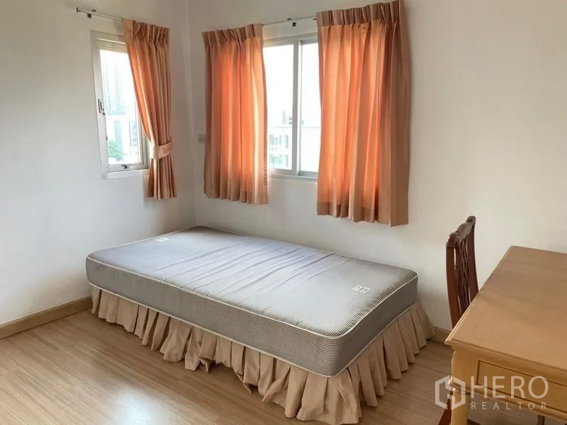 Condominium for rent in Khlong Toei, Bangkok - Cozy single bedroom with desk, corner windows, and peach curtains bringing in natural light.
