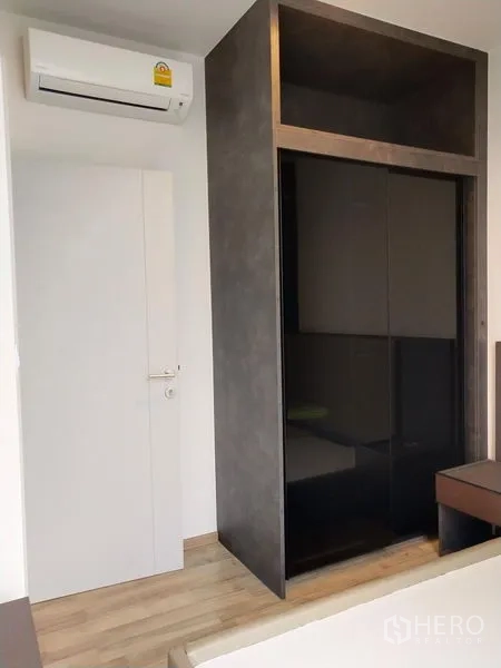 公寓 出租在Chatuchak, Bangkok - 卧室角落，黑色亮面推拉衣柜与壁挂空调。