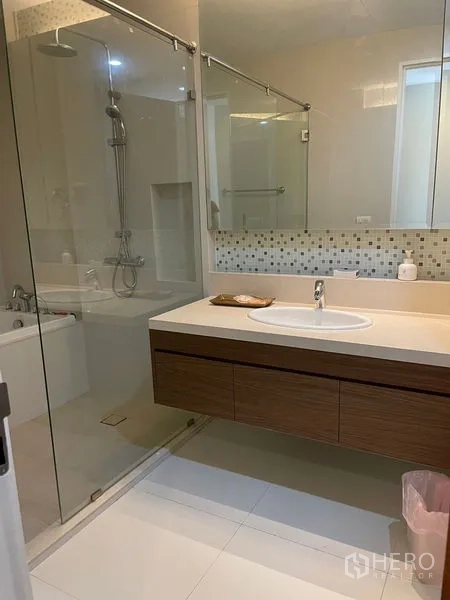 Condominium for rent in Khlong Toei, Bangkok - Spacious bathroom with glass-enclosed shower, bathtub, large mirror, and floating vanity.