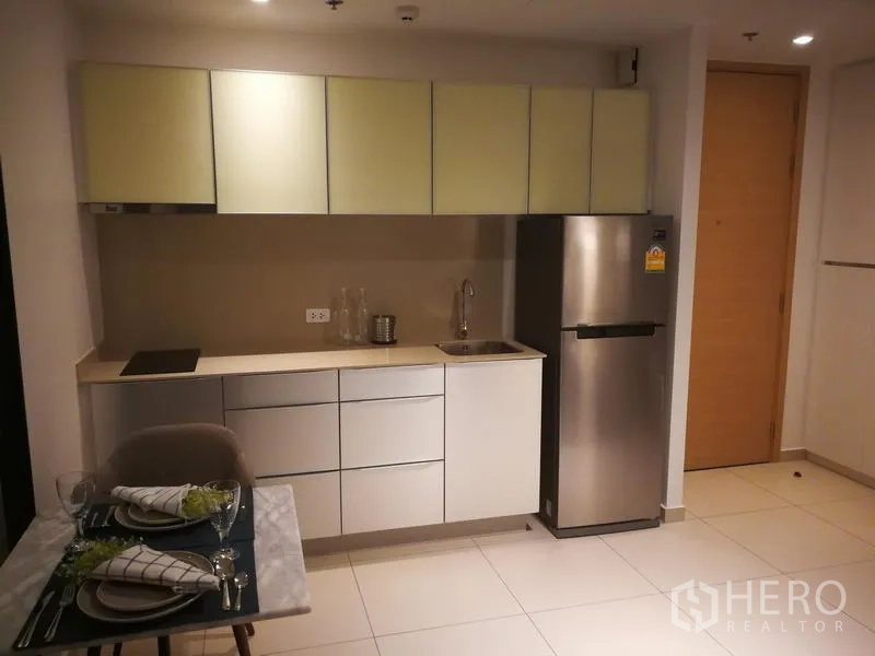 公寓 出租或出售在Watthana, Bangkok - 内置厨房柜体配灶台、水槽和冰箱，旁边是精巧餐桌。
