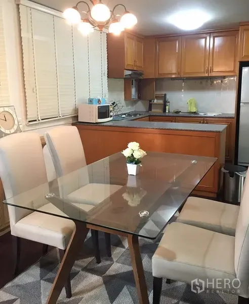 Condominium for rent in Watthana, Bangkok - Bright dining area with a glass table and upholstered chairs beside a wood-fitted kitchen in a Bangkok condo.
