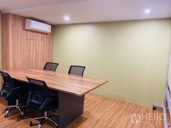 Office Space for rent in Bang Rak, Bangkok - Conference room with a long wooden table, mesh chairs, air conditioning and a soft green wall.