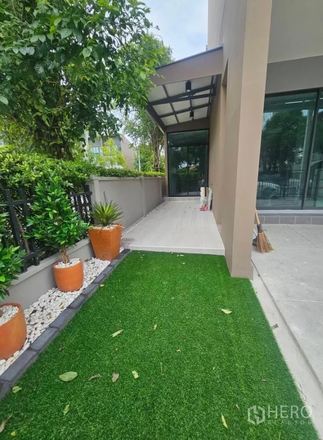 Townhouse for rent in Saphan Sung, Bangkok - Corner garden with artificial grass, potted plants and walkway to the house.