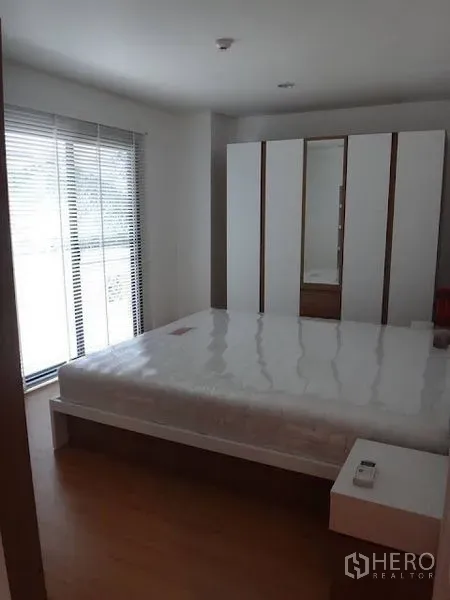Condominium for rent in Bang Rak, Bangkok - Bright bedroom with queen bed, floor-to-ceiling windows with blinds, and a white wardrobe on wood floors.