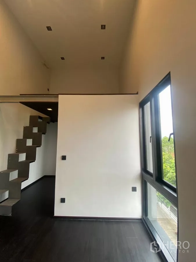 Townhouse for rent in Huai Khwang, Bangkok - High-ceiling room with a loft platform and sculptural metal staircase.