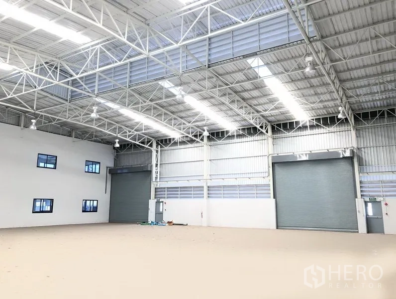 Factory for rent or sale in Bang Sao Thong, Samut Prakan - Open warehouse hall featuring two large roller shutter doors, ventilation louver panels and bright skylights.