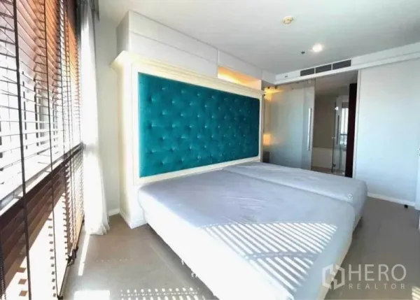 Condominium for rent in Khlong San, Bangkok - Sunlit bedroom with teal tufted headboard and a glass door to the ensuite bathroom.
