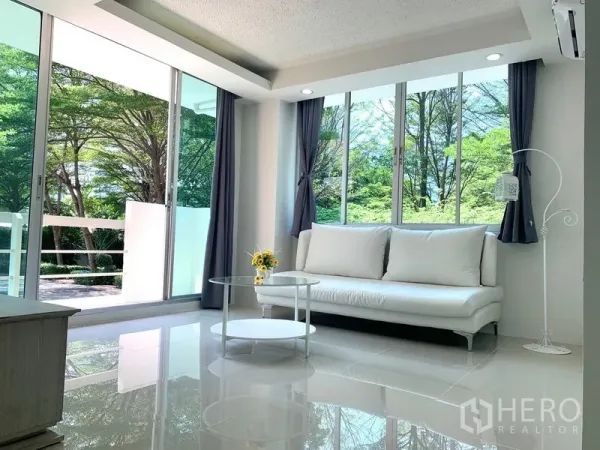 Condominium for rent or sale in Khlong Toei, Bangkok - Corner living area with white sofa, round glass coffee table and floor-to-ceiling windows to trees.